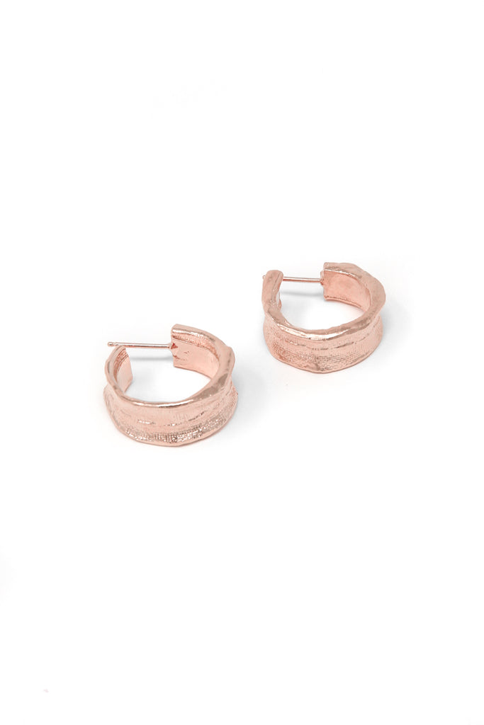 Small hand-stitched huggie earring in 14k rose gold. Huggie hoop earrings with a textured surface created by casting fabric into metal. Handmade by local jewelry designer, Nina Berenato, in Austin, Texas.